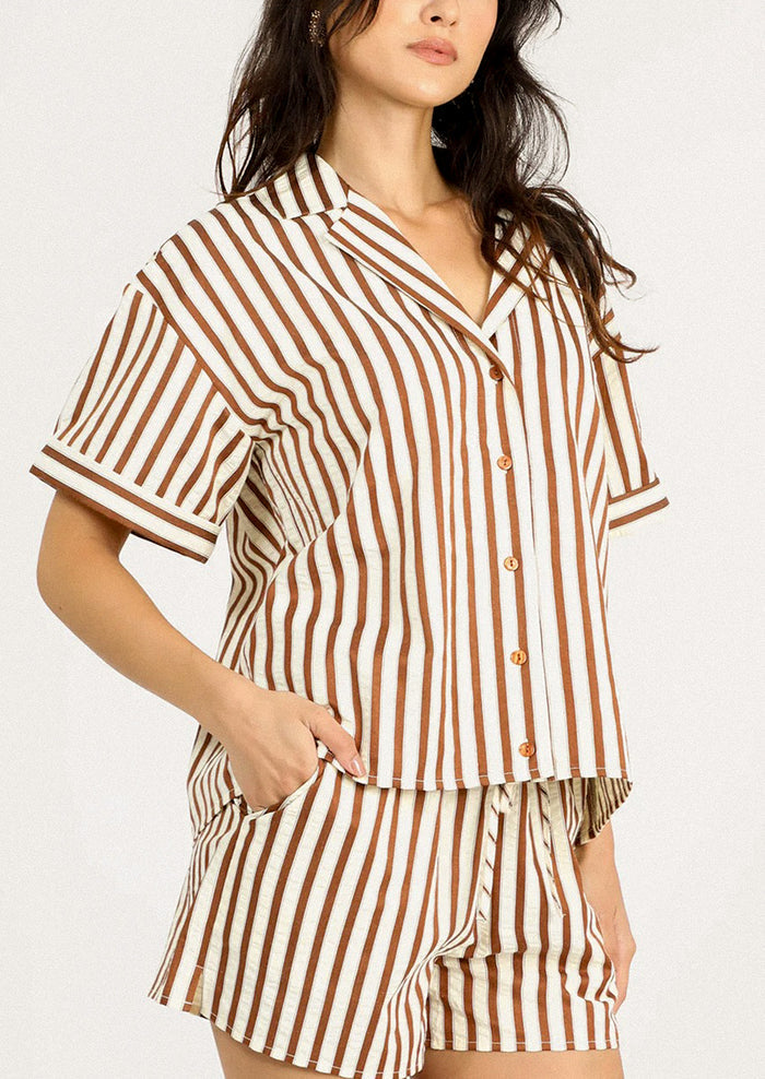 A person wearing a short sleeve button front shirt in cream and brown stripe.